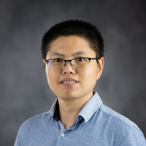 Portrait of Kaili Cao: a smiling man with short black hair and glasses, in a blue striped shirt, against a gray background.